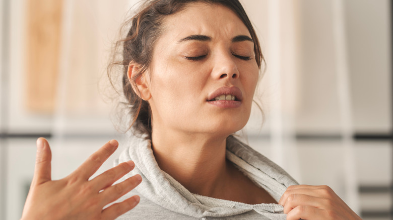 A young woman fans her face with her hand, showing signs of discomfort in hot weather