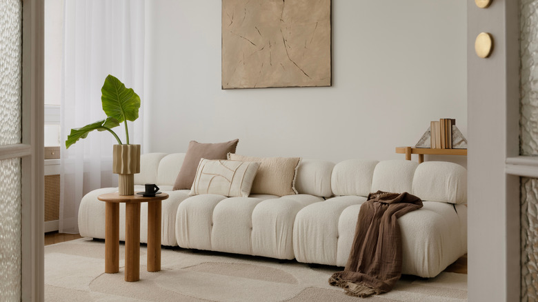 White modular couch in a neutral living room with a green plant and wooden tables