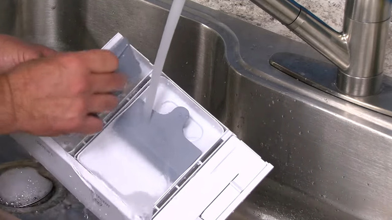 Man washing a laundry detergent tray in the sink