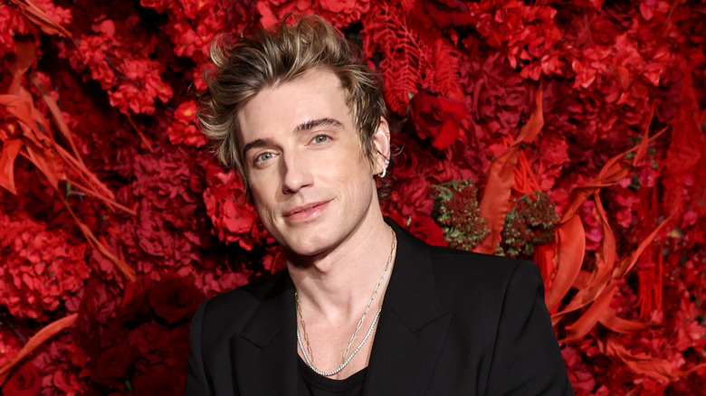 Jeremiah Brent wearing all black and posing at an upscale event, standing in front of a floral wall with rich red colors.
