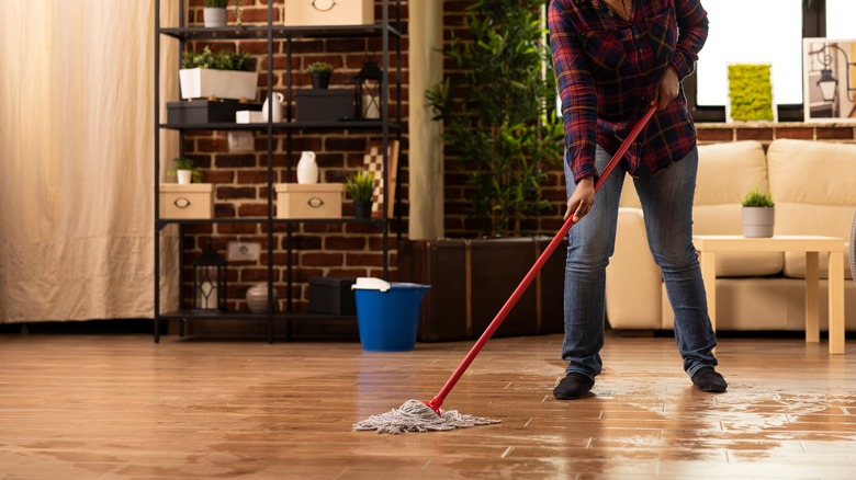 A traditional mop and bucket are used to clean hardwood floors in a largely brick apartment space.