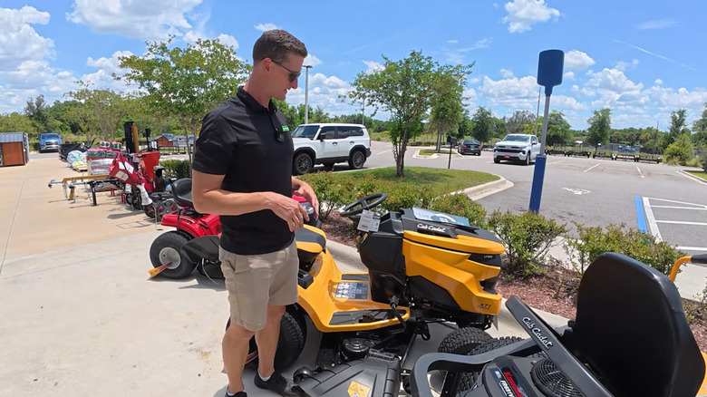 A man looking at zero-turn mowers lined up near a parking lot next to a Tractor Supply Co. store
