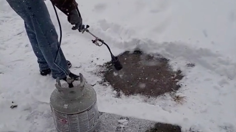 person in jeans using a blow torch to melt snow on driveway