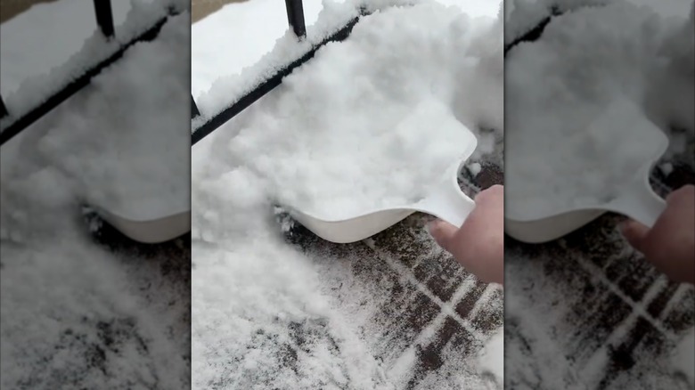 person holding a white dust pan and picking up snow