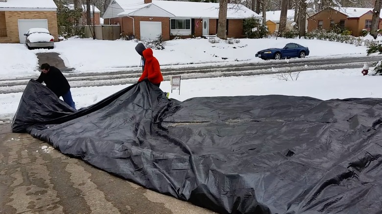 three people pulling a black tarp