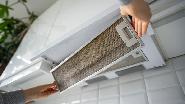 A person removing a filter from a vent hood