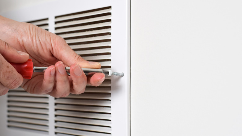 A person unscrewing a return air vent cover