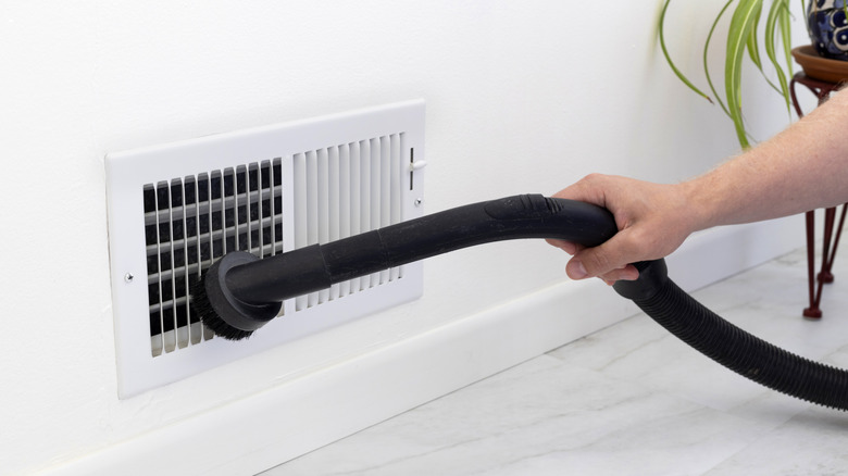 A person using a vacuum to clean a vent