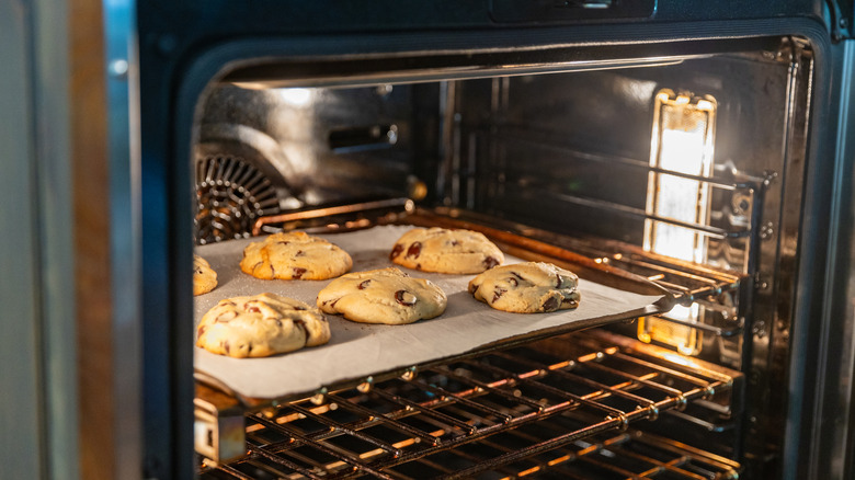 An open oven with the light on and chocolate chip cookies inside