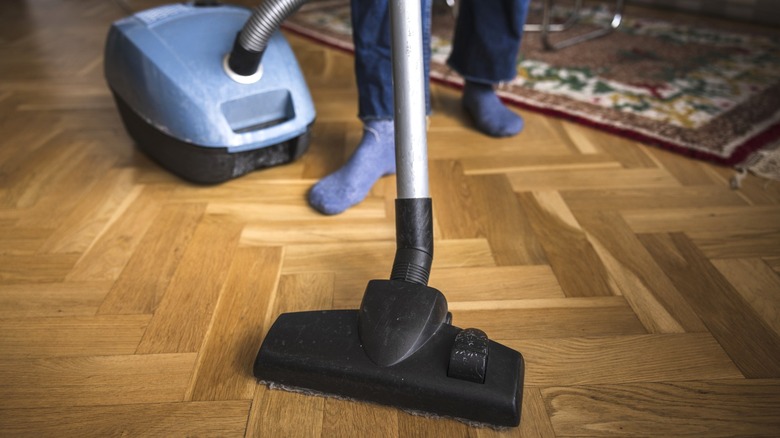 Person vacuuming herringbone parquet floor with canister vauum