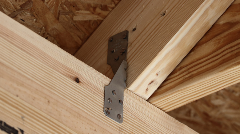 A close-up of a metal hurricane strap secured to wooden roof framing with nails