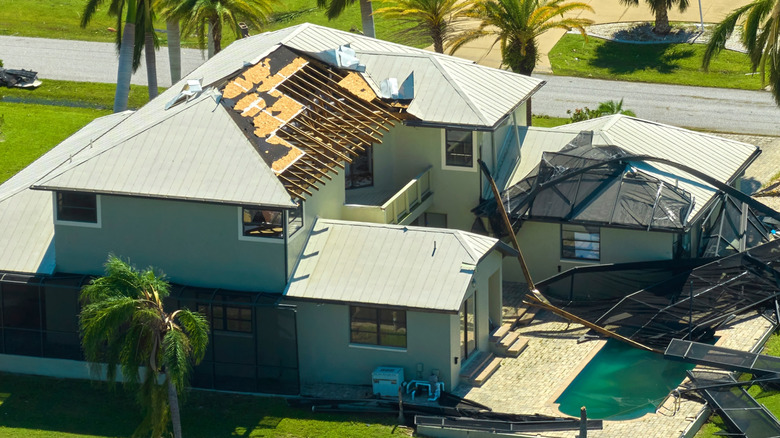 A house with part of roof blown away and pool screen destroyed