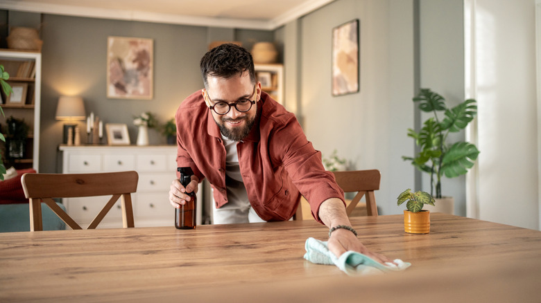A man wipes a table using a cloth and liquid from a spray bottle
