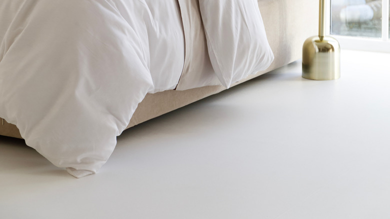 Cozy, comfortable bed with thick comforter and lots of pillows and flowers in a vase on the side table