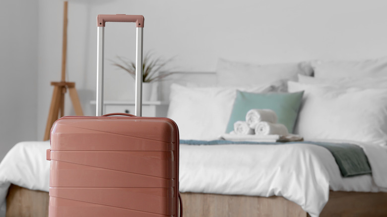 A suitcase sitting in front of a freshly-made bed with guest towels stacked on top