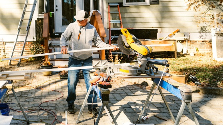 A contractor surrounded by power tools works in front of a house on fencing material