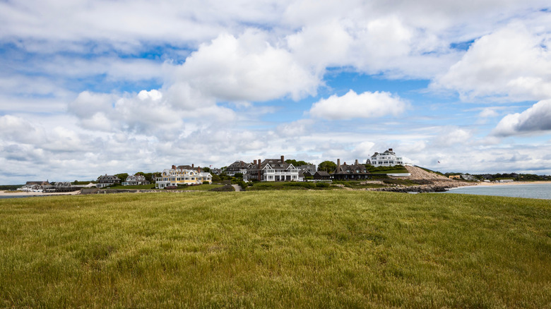 Taylor Swift's Watch Hill home in Rhode Island with other houses in the neighborhood to the left, blue sky, clouds, and grass in the foreground