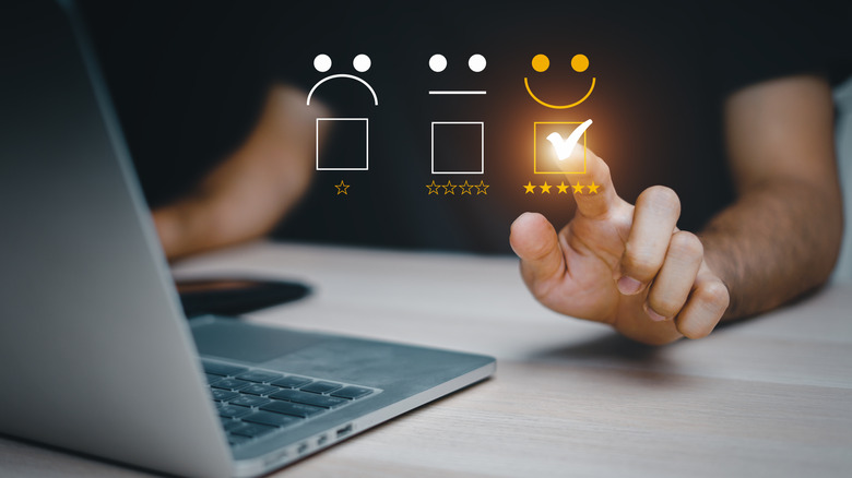 Person sitting behind a laptop with a sad face, straight face, and happy face icons over the image and the persons hand selecting the happy face