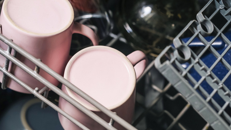 Two pink coffee mugs on the top rack of a dishwasher with a blue bowl on the bottom rack in the background