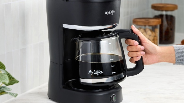 Person reaching for carafe from Mr. Coffee drip coffee maker