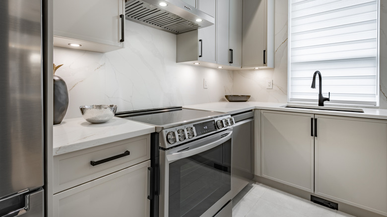 Kitchen interior with grey cabinets with white marble, range oven, with stainless vent hood, sink with black faucet.