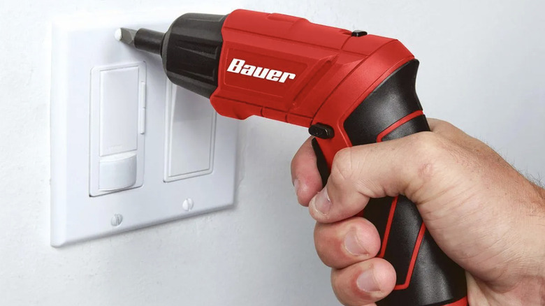 A person using an electric screwdriver on a light switch cover