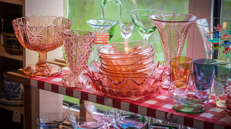 Many colors of vintage Depression glass are on display near a window.