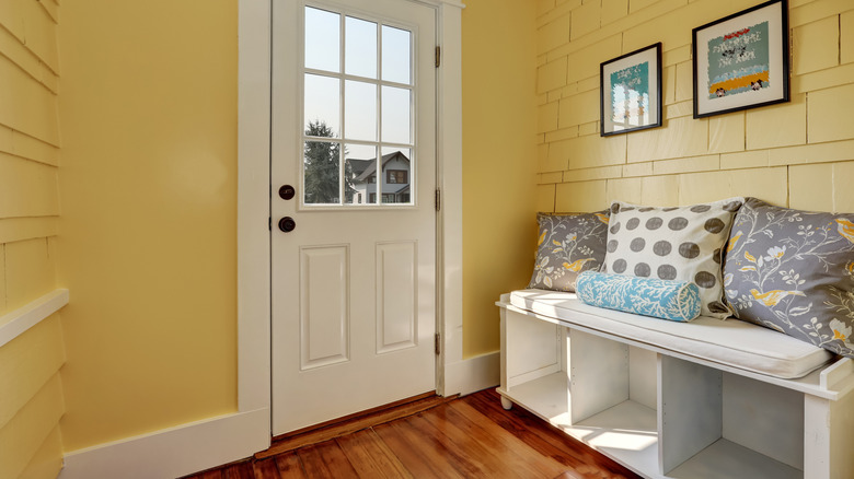 Entryway area with yellow walls, white front door, and white storage bench