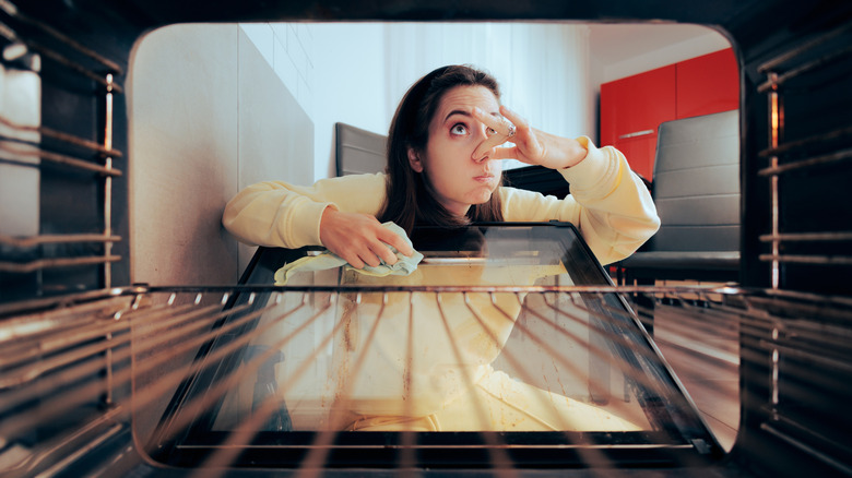Woman holding her nose while cleaning oven