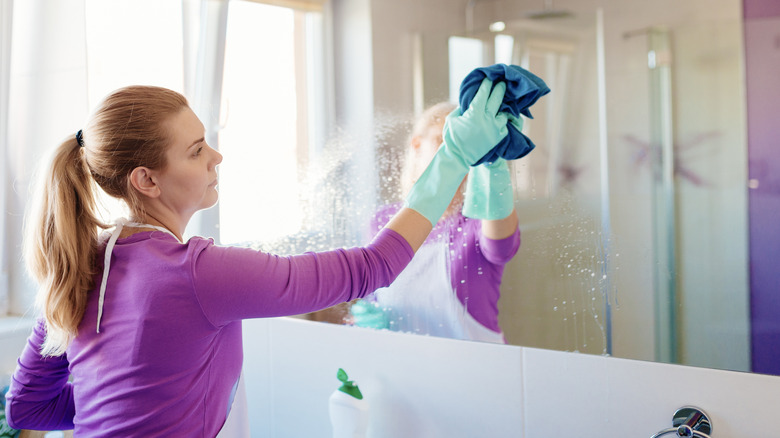 Woman cleaning bathroom mirror