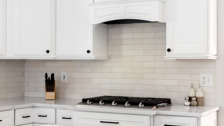 White kitchen with stove, cabinets, and white subway tile.