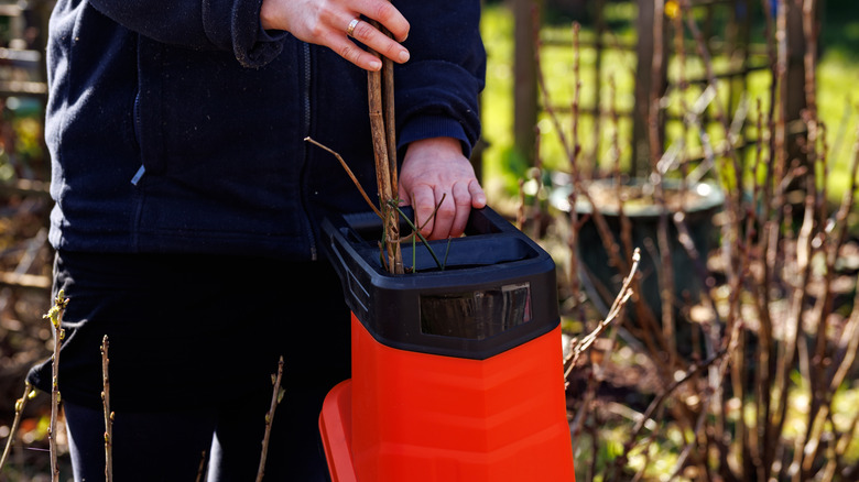 Grasses and twigs are being inserted into the top of an orange leaf mulcher