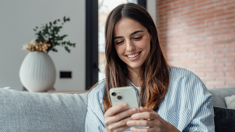 Young girl sitting on couch and smiling while looking on her phone