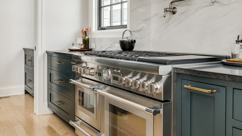 Transitional kitchen with deep blue lower cabinets next to a sleek gas oven