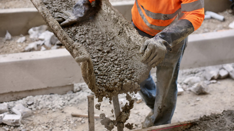 person wearing blue jeans and an orange reflective vest pouring concrete