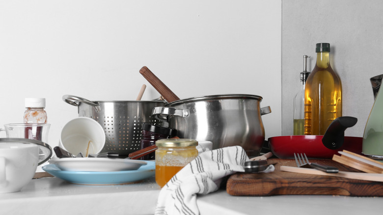 A messy kitchen countertop with dishes and food containers littered throughout