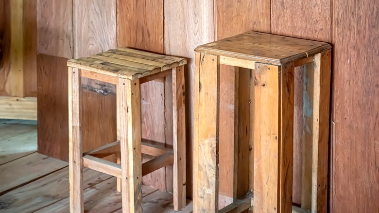 A pair of old wooden stools against a wood wall