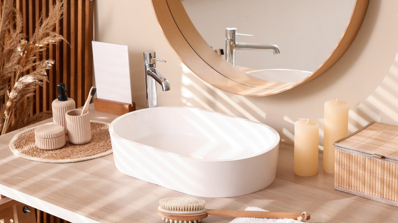 a round mirror with wood tones over a non-traditional vanity sink
