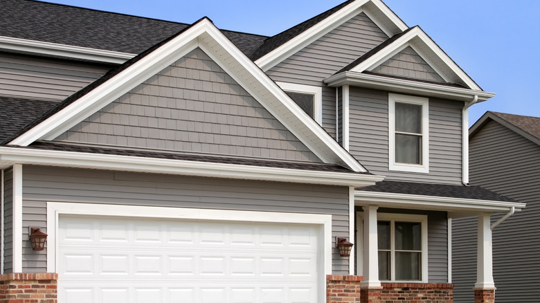 Two-story home with gray vinyl siding and white trim, a white garage door and brick accents also visible