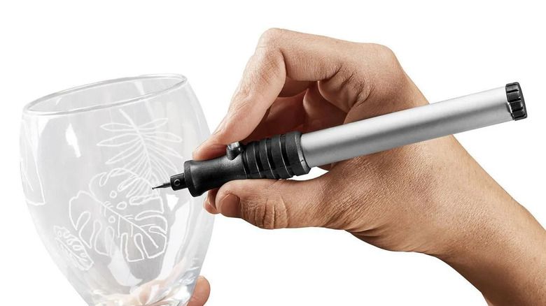A close-up of someone using a micro-engraver to add custom etching to a wine glass.