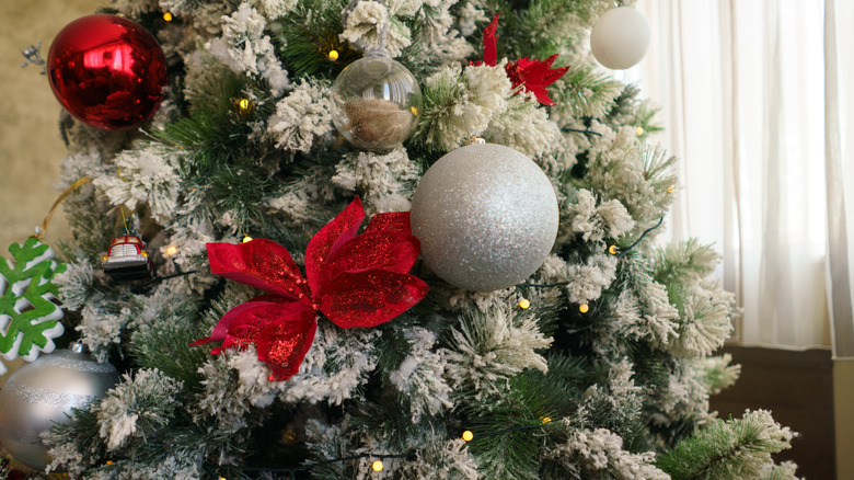 Closeup of a flocked Christmas tree with red and silver baubles and a red bow