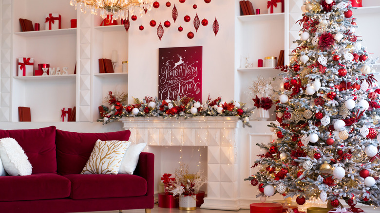 A living room decorated for Christmas with a large tree, garland on the mantel, and gifts on the shelves