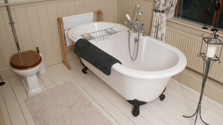 White clawfoot bathtub with bath mat and tub tray