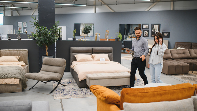 A shopper walks with a store clerk through a shop floor filled with bedroom furniture.