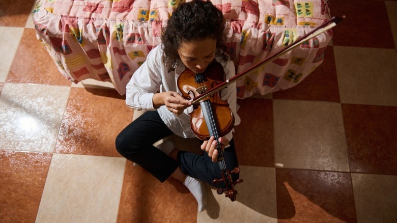 Woman sitting on a brown and white checkered floor playing violin