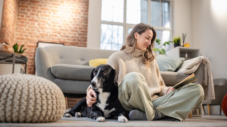 A woman sitting on floor reading with her dog
