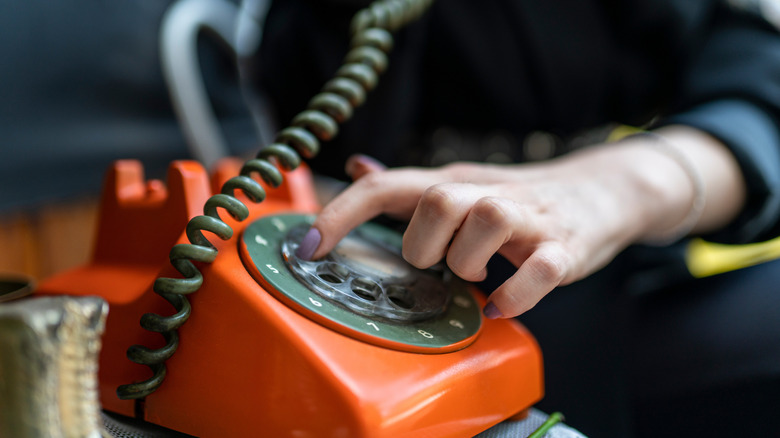 woman's hand dialing on an orange rotary phone