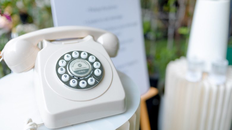A rotary phone on a table in front of wedding decorations with a label that says "greetings record your memory"