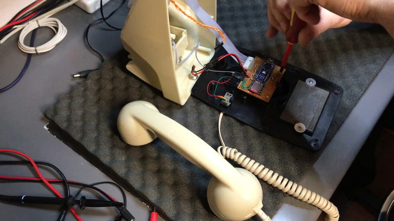 hands tightening a screw on a modern sound board inside a rotary phone