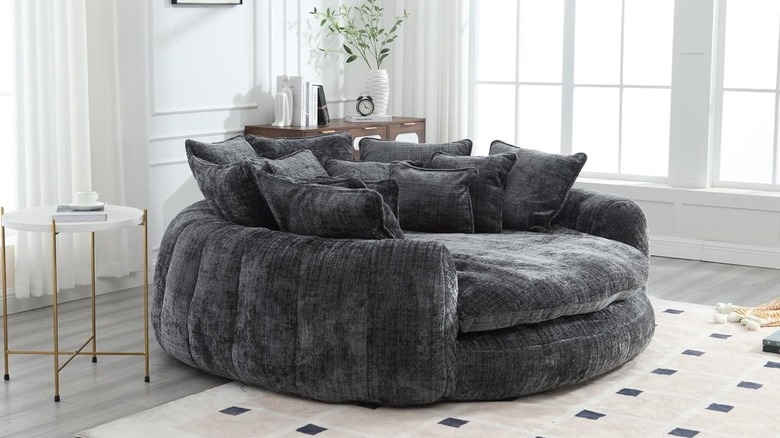 A dark gray circular daybed, full of matching pillows